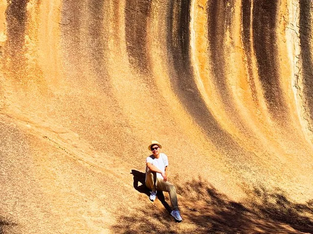 A person sitting on the curved, striped rock face of Wave Rock.