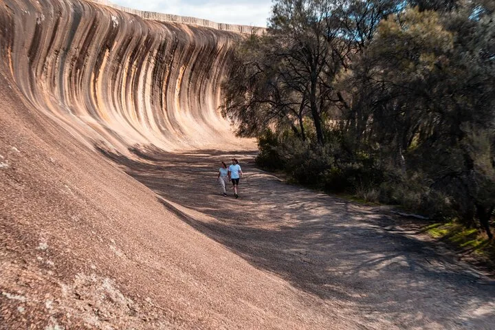 Zwei Personen, die am Fuß des Wave Rock in Westaustralien entlanggehen.
