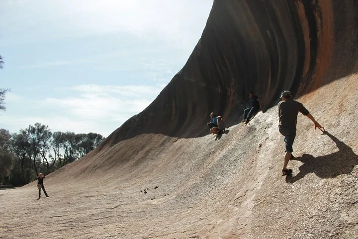 Menschen klettern und sitzen auf der schrägen Oberfläche des Wave Rock.