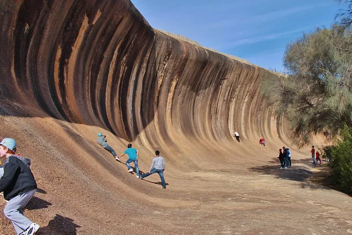 Mehrere Personen klettern an der steilen Wand des Wave Rock und erkunden sie.