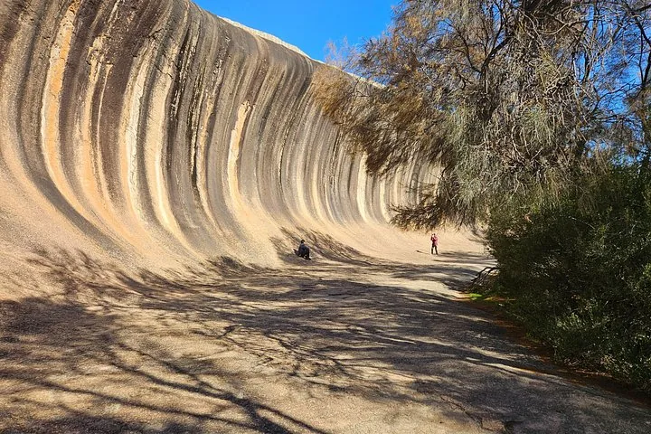 Ein paar Personen erkunden den sandigen Fuß des gewaltigen Wave Rock.